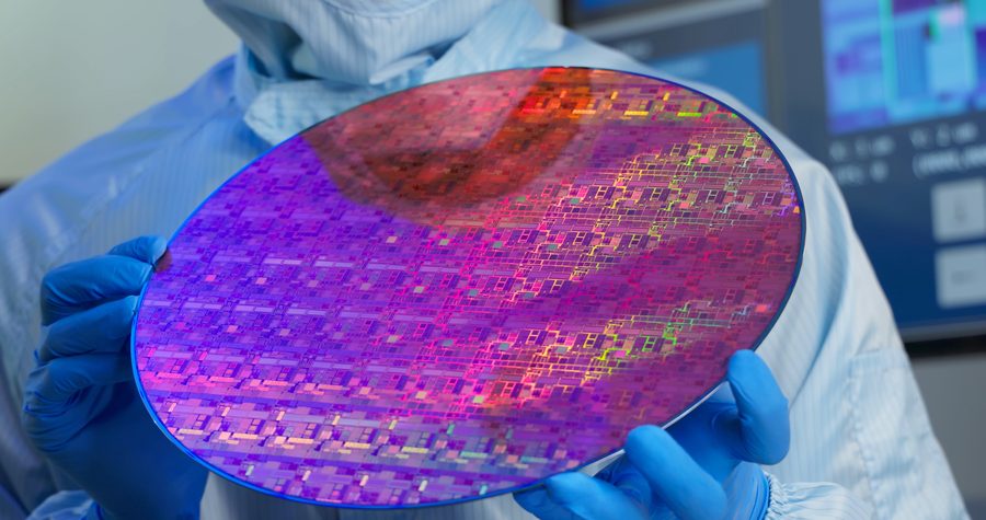 Technician in a cleanroom suit holding a semiconductor wafer